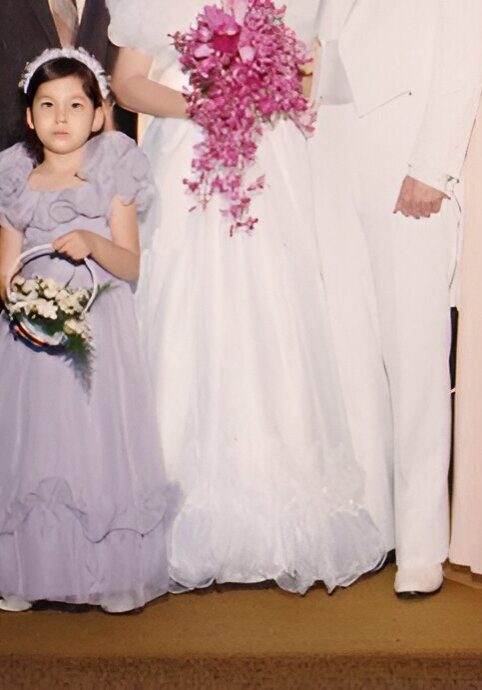 A young girl in a purple dress holding flowers.